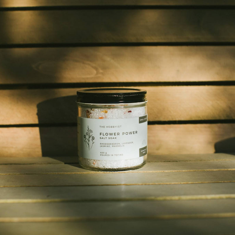 Candle labeled 'Flower Power' on a wooden surface with a warm glow