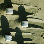 three cylindrical containers with labels on a sandy surface