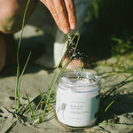Person pouring water from a bottle into a jar labeled 'Doze' on a sandy surface with grass.
